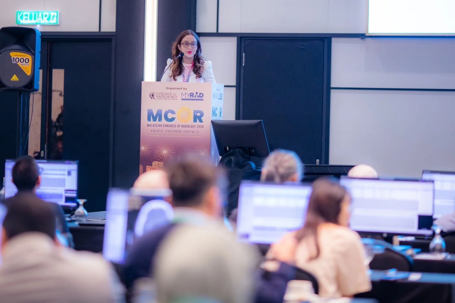 Dr Farhana Fadzli at the MCoR lectern, with an audience and computer workstations in the foreground